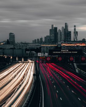 Night cityscape featuring skyscrapers and dynamic light trails on highways under an overcast sky.