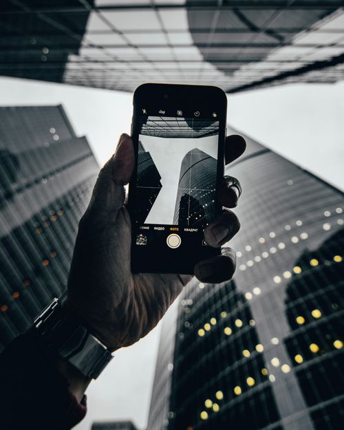 Free A hand holding a smartphone captures a dramatic perspective of city skyscrapers. Stock Photo