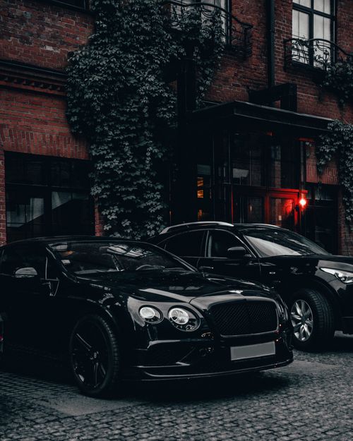 Free Elegant luxury black sports car parked outside a stylish urban building with ivy-covered walls. Stock Photo