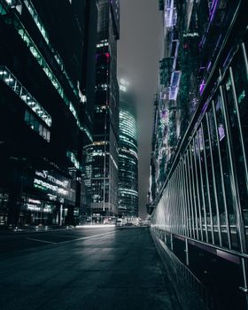 A moody nighttime scene showcasing modern skyscrapers lit up in an urban cityscape.