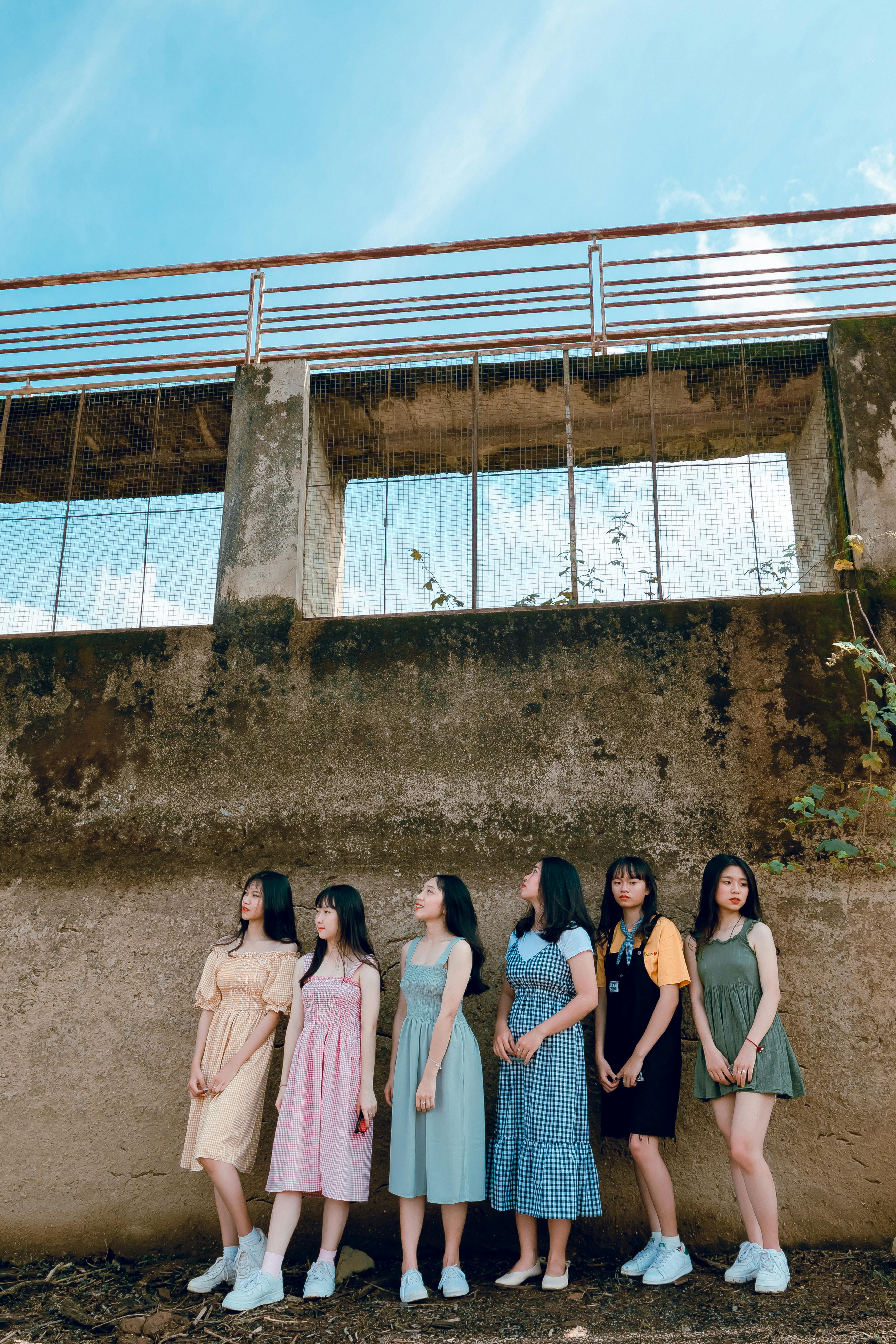 六名年轻女子并肩站在户外，倚靠着饱经风霜的墙壁