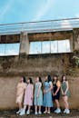 六名年轻女子并肩站在户外，倚靠着饱经风霜的墙壁