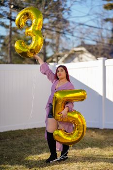 Woman holding gold 35 balloons in a garden celebration on a sunny day.