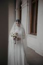 Beautiful Bride in White Wedding Dress and Veil Looking at Bouquet of Flowers 