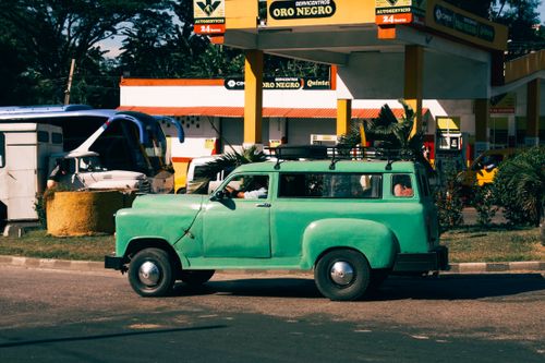Free A vintage green truck parked at a retro-style gas station with palm trees and colorful signage. Stock Photo