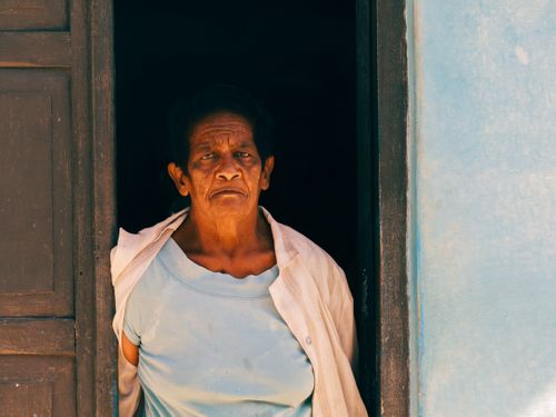 Free Senior woman standing in a doorway, wearing a light blue shirt and looking forward. Stock Photo