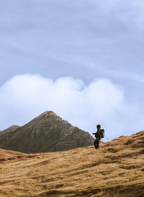 Man in Black Jacket and Pants Walking on Brown Field Near Mountain 