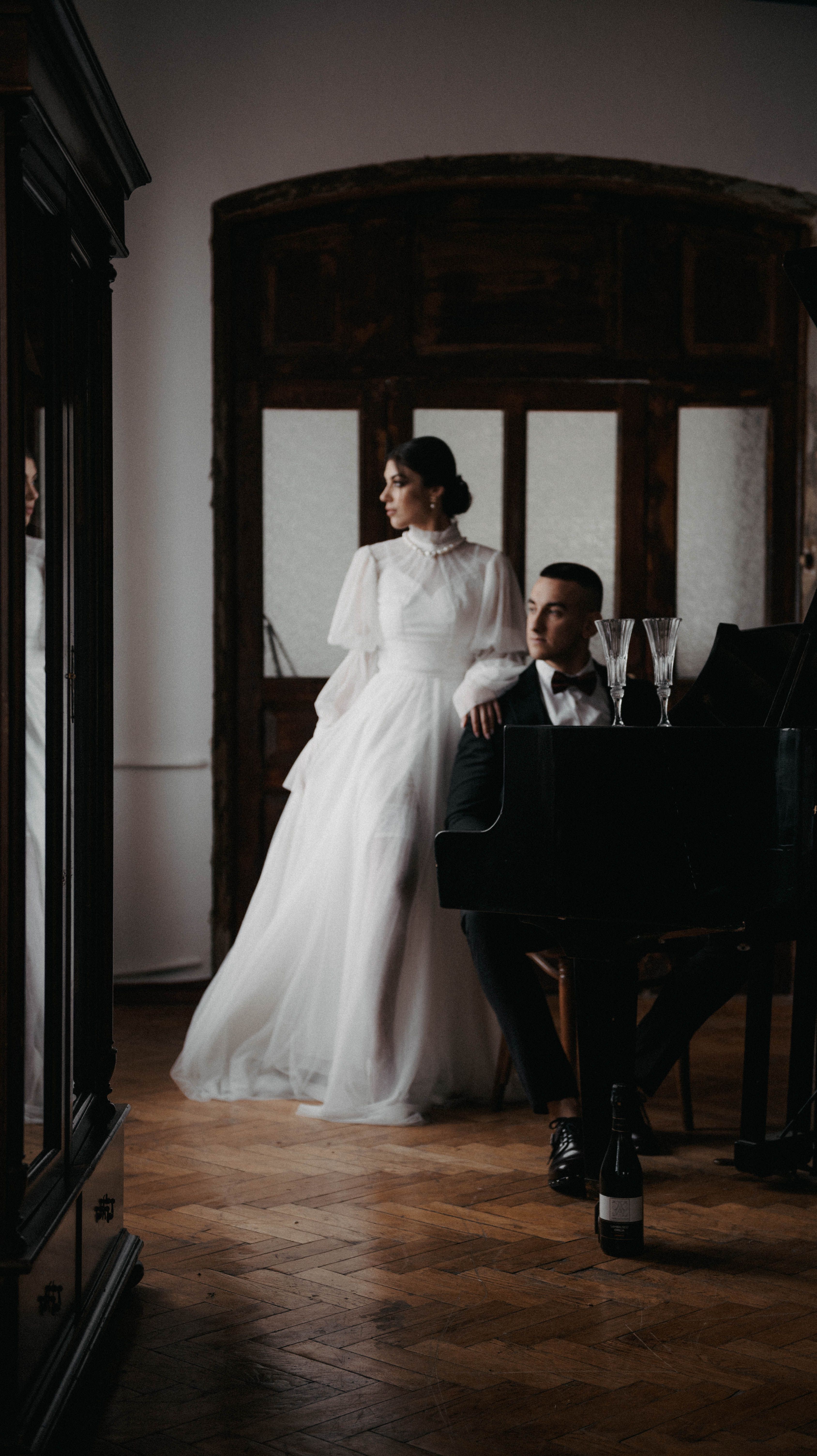 Bride in lace dress and groom at piano create timeless elegance in an indoor wedding scene.