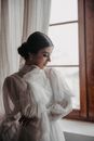 Woman in White Long Sleeve Shirt Standing Near Window
