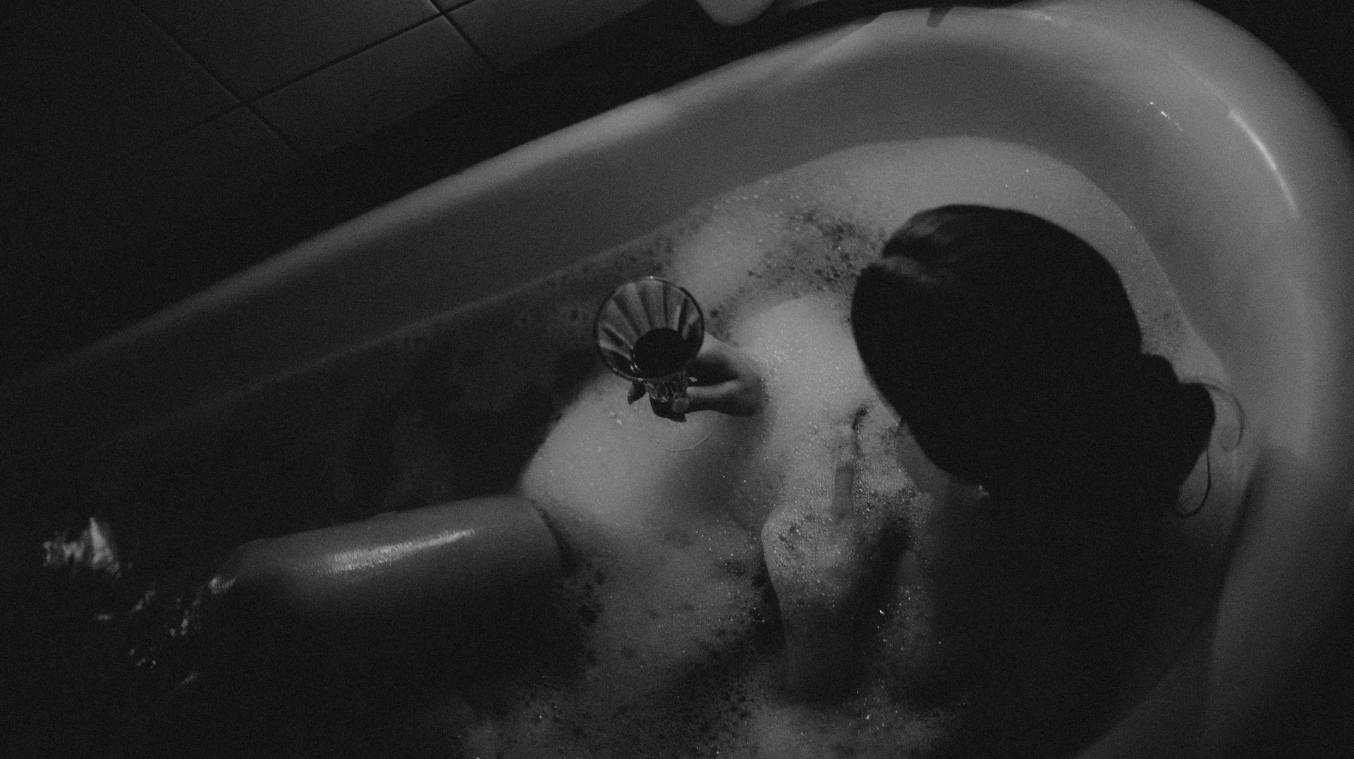 Monochromatic view of a woman enjoying a bath with a glass of wine, a serene and intimate moment.