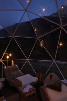 Relax inside a warm dome with plush seating and a night view of mountains through glass panels.