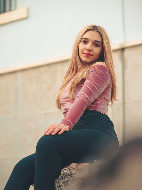 Free Young woman with long blonde hair posing outdoors in a pink velvet top and black pants. Stock Photo