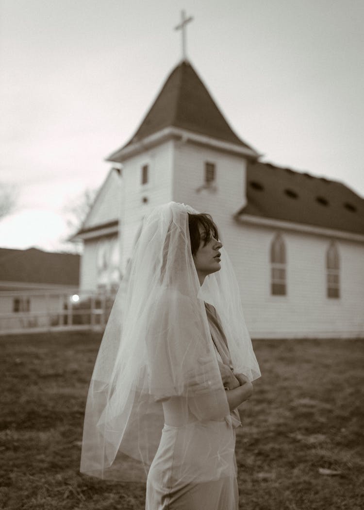 Bride In White Wedding Dress And Veil Waiting Before Country Church