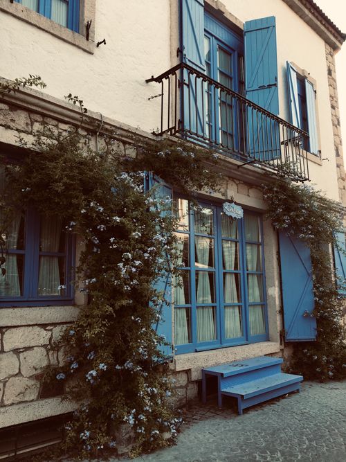 Free A picturesque house with blue shutters and vibrant flowers in Alaçatı, Turkey. Stock Photo