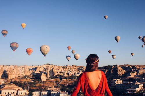 A Back View of a Woman Looking at the Hot Air Balloons Under the Blue Sky