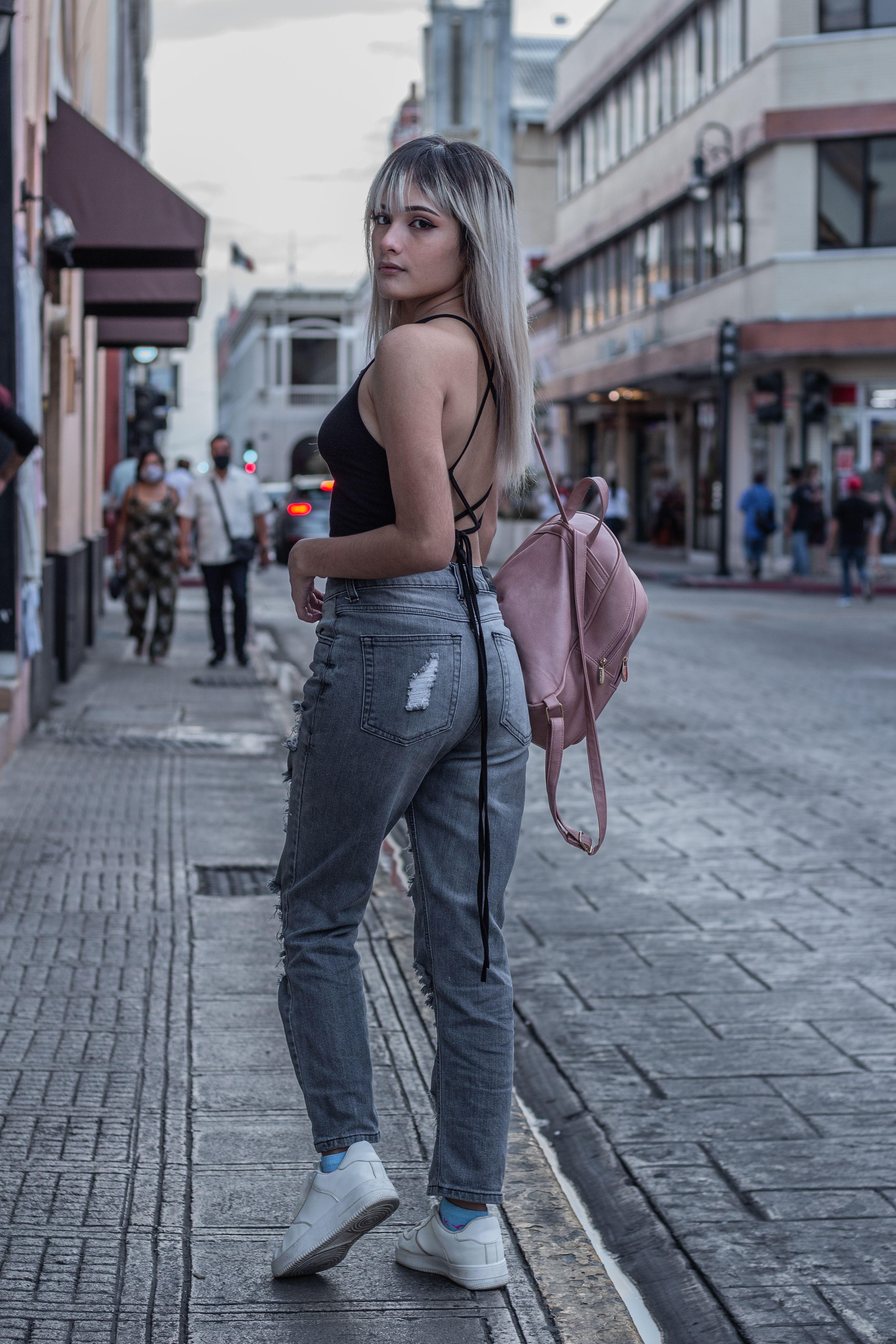 Uma mulher estilosa com cabelo colorido e uma mochila em uma calçada da cidade, exibindo moda urbana.