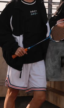 Person holding badminton racket in a casual urban setting, dressed for sport.