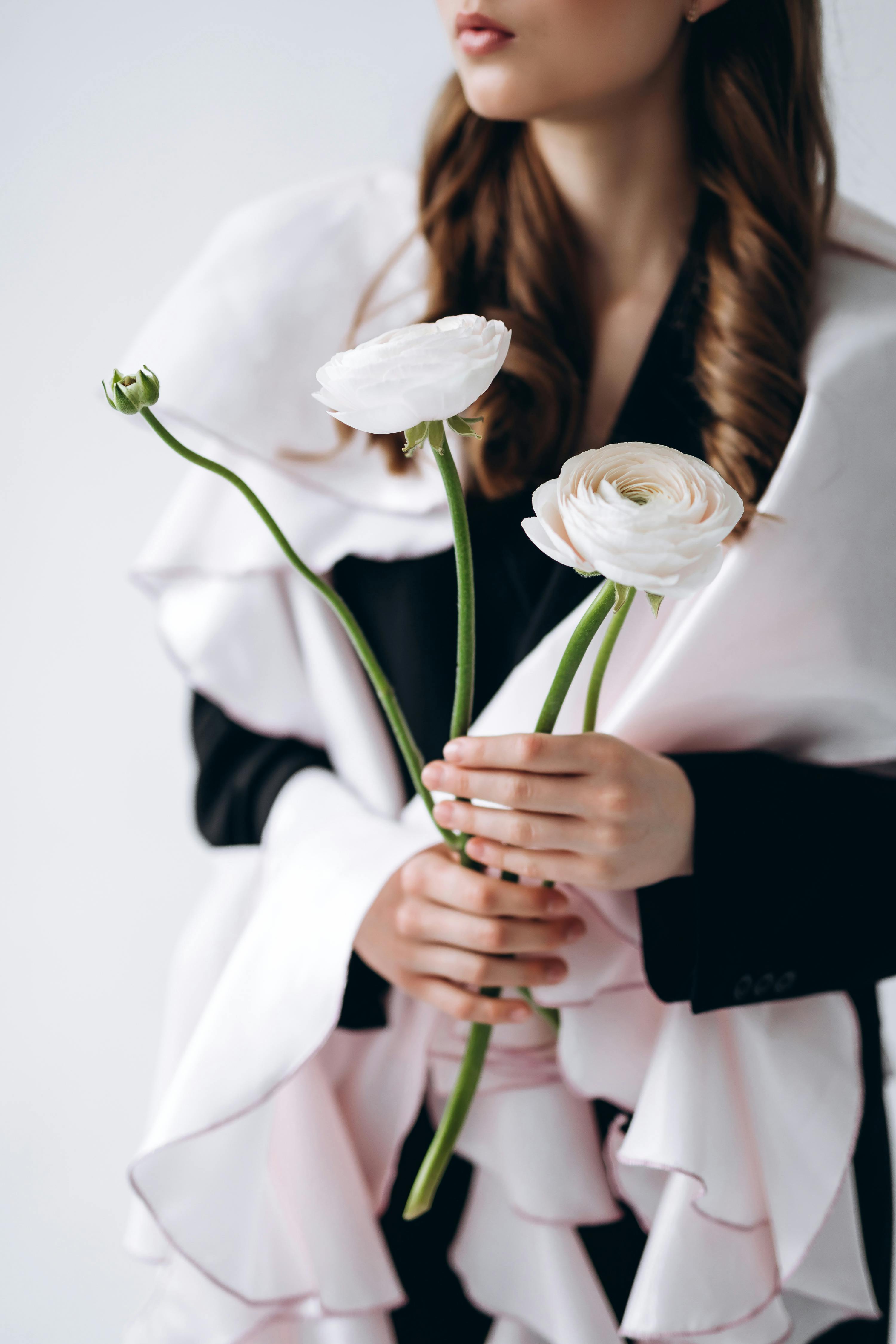 Portrait of a woman holding white ranunculus flowers in elegant, layered clothing.