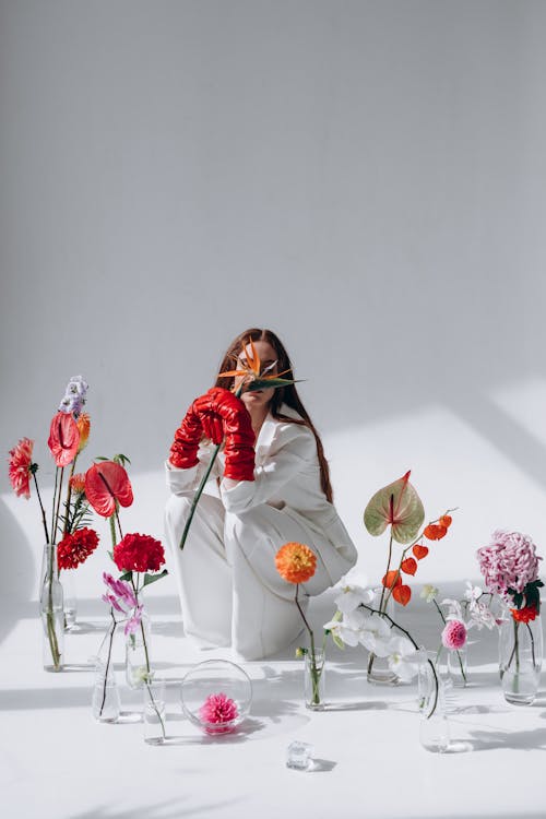 Woman in White Crouching Among Flowers in Vases