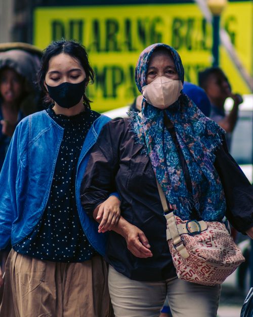 Free Two women in masks walking on a busy city street, capturing the urban life during pandemic. Stock Photo