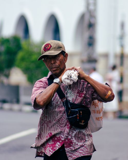 Free Elderly man with a cap carrying sack on street, showing resilience and determination. Stock Photo