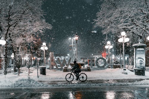 A Person Riding a Bike on the Street at Night while Snowing