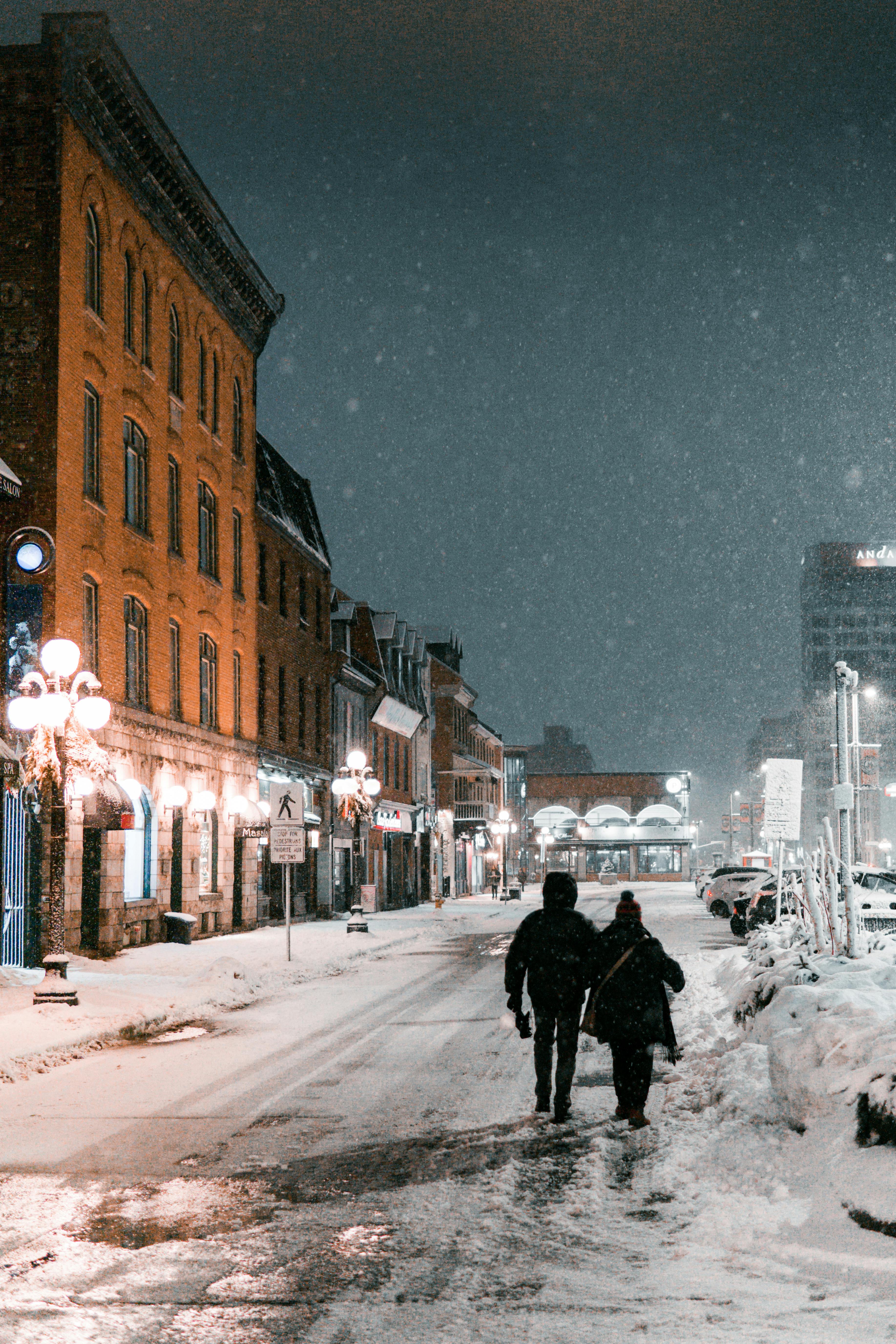 A couple walks along a snow-covered street in Ottawa, Canada, illuminated by street lamps on a winter night.