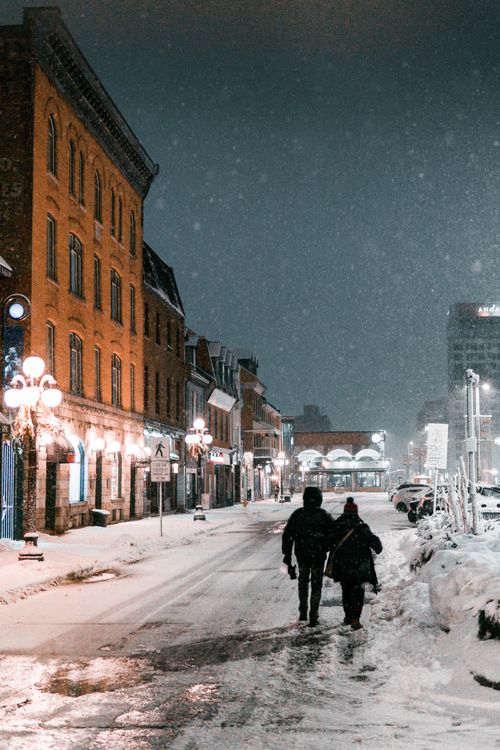 Free A couple walks along a snow-covered street in Ottawa, Canada, illuminated by street lamps on a winter night. Stock Photo