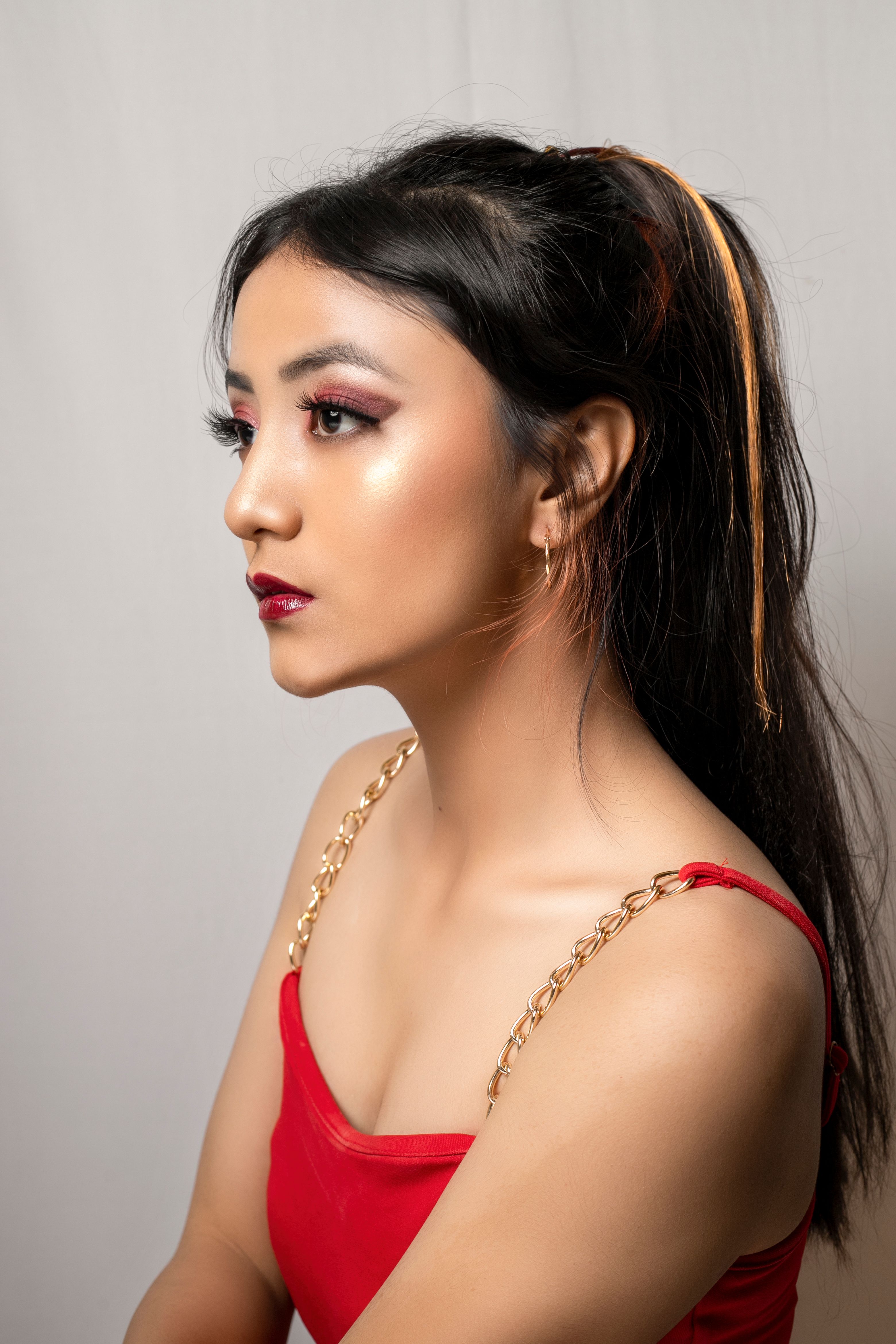 A stunning side profile portrait of a young woman with makeup, dressed in a red outfit.