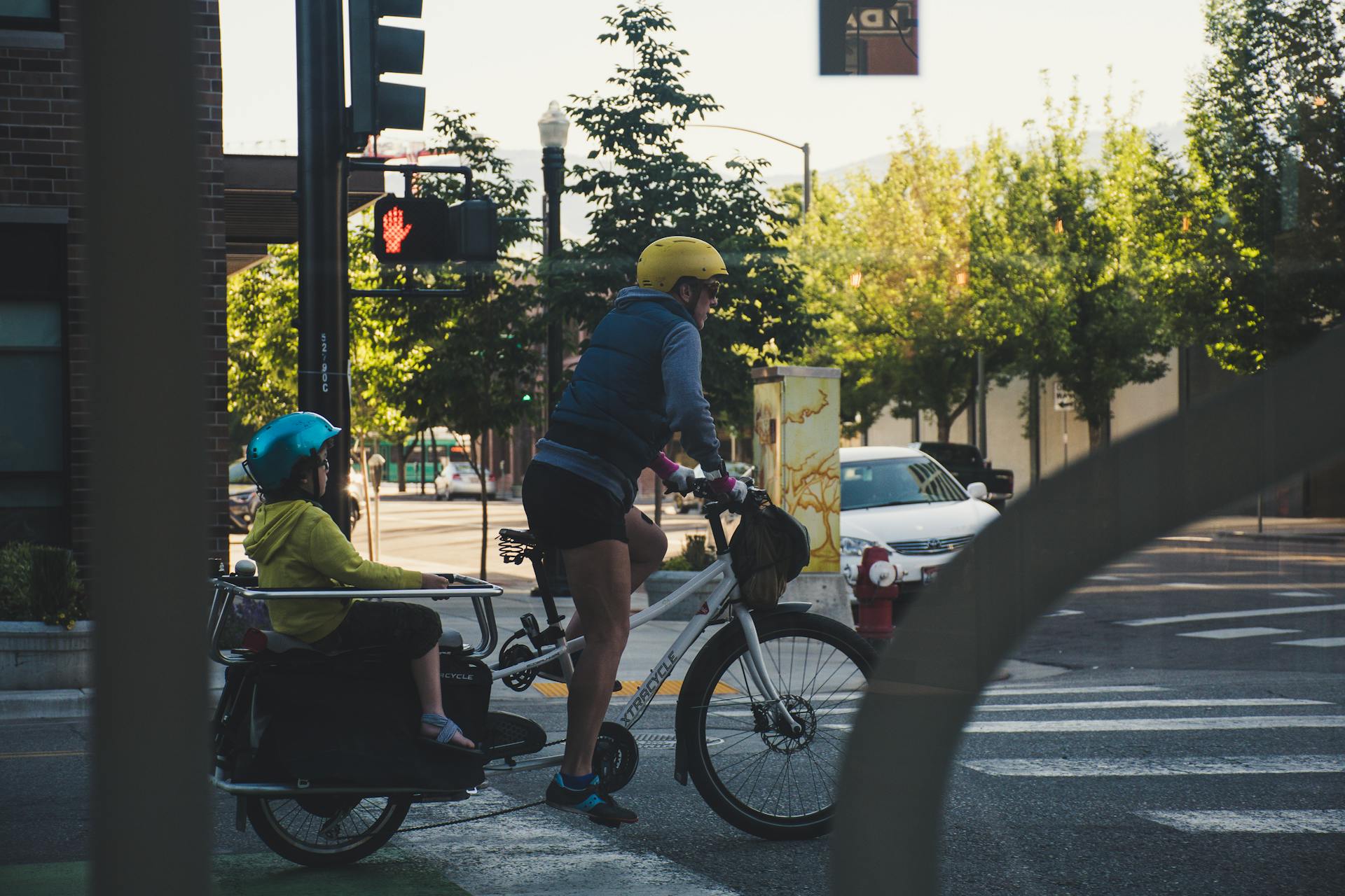 Cyclist with child carrier bike stopped at urban intersection during daylight.