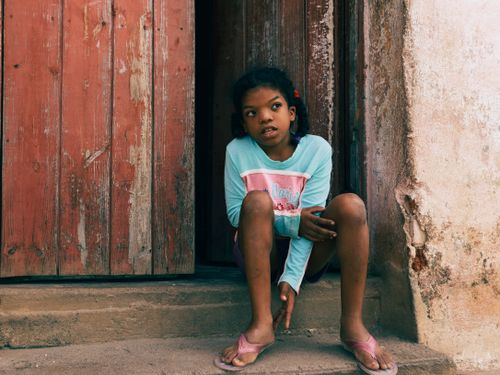 Free A young girl sitting at a rustic wooden doorway, lost in thought. Stock Photo