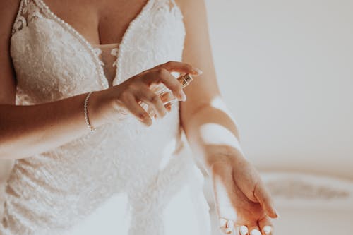 Unrecognizable Woman in White Lacy Dress Spraying Perfume on Wrist