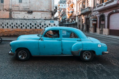 Free A vintage blue car cruises the weathered streets of a historic city, exuding classic charm. Stock Photo