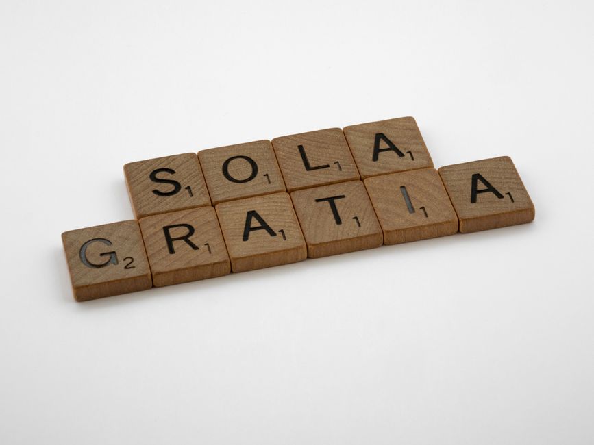 Wooden Scrabble tiles arranged to spell 'Sola Gratia' on a white surface.