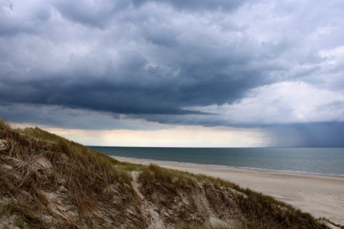 Free Stormy clouds gather over the sandy shores of Lønstrup Beach, creating a moody seascape in Denmark. Stock Photo