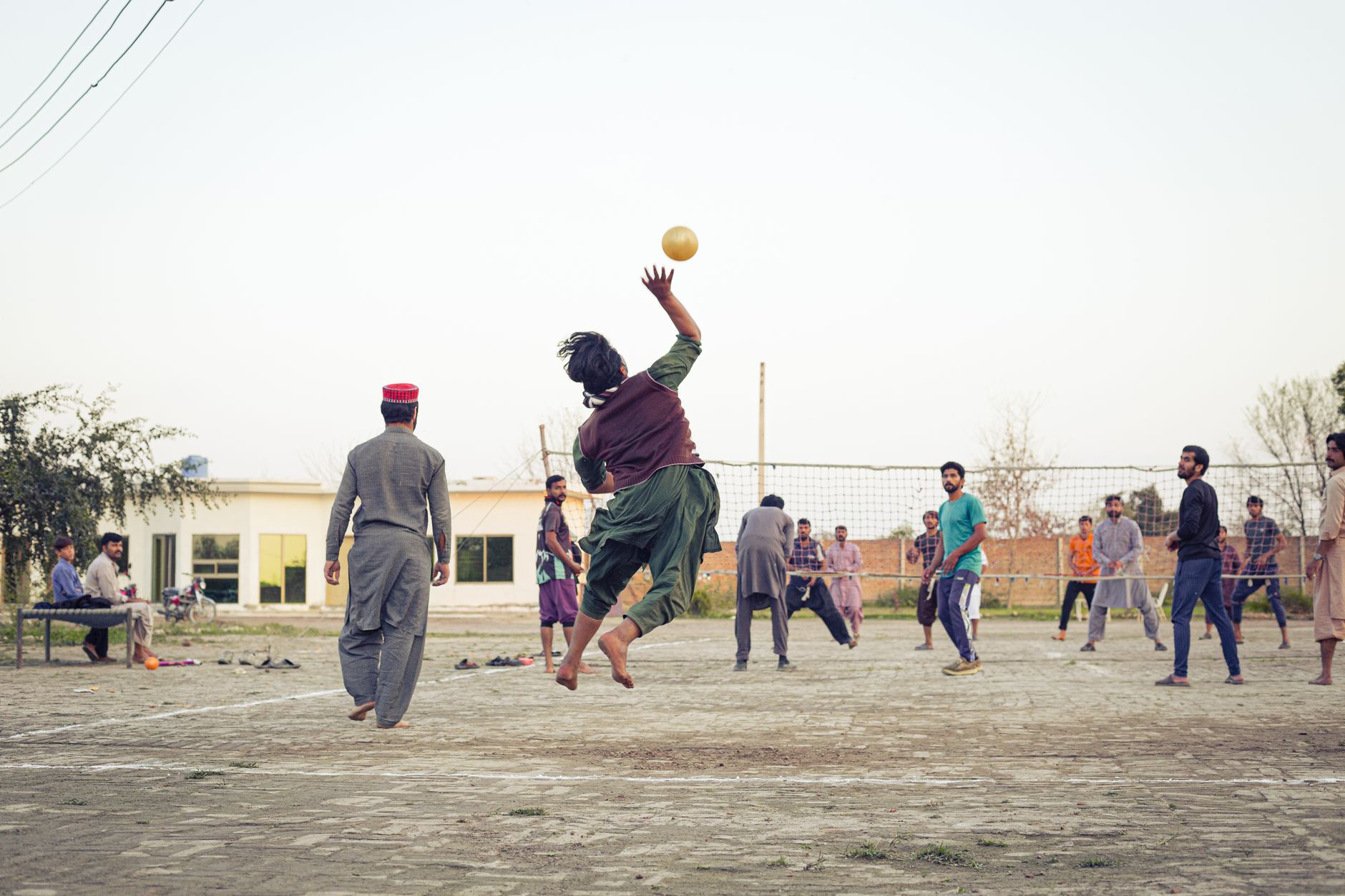 A dynamic scene of men playing volleyball outdoors at dusk, showcasing athleticism and teamwork.