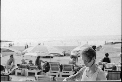 Grayscale view of people relaxing on the beach under umbrellas on a sunny day.