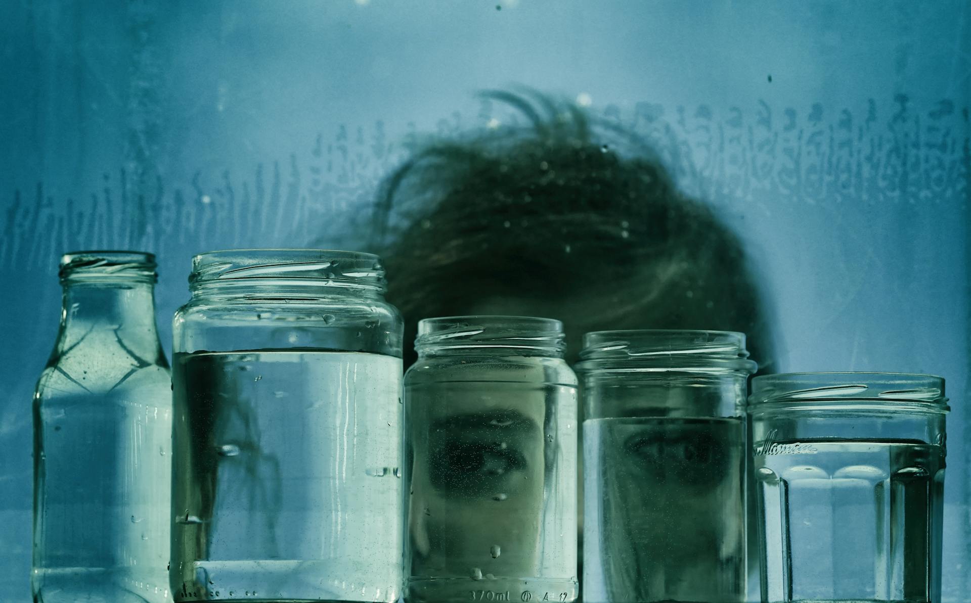 Person Looking From Behind Jars Filled with Water
