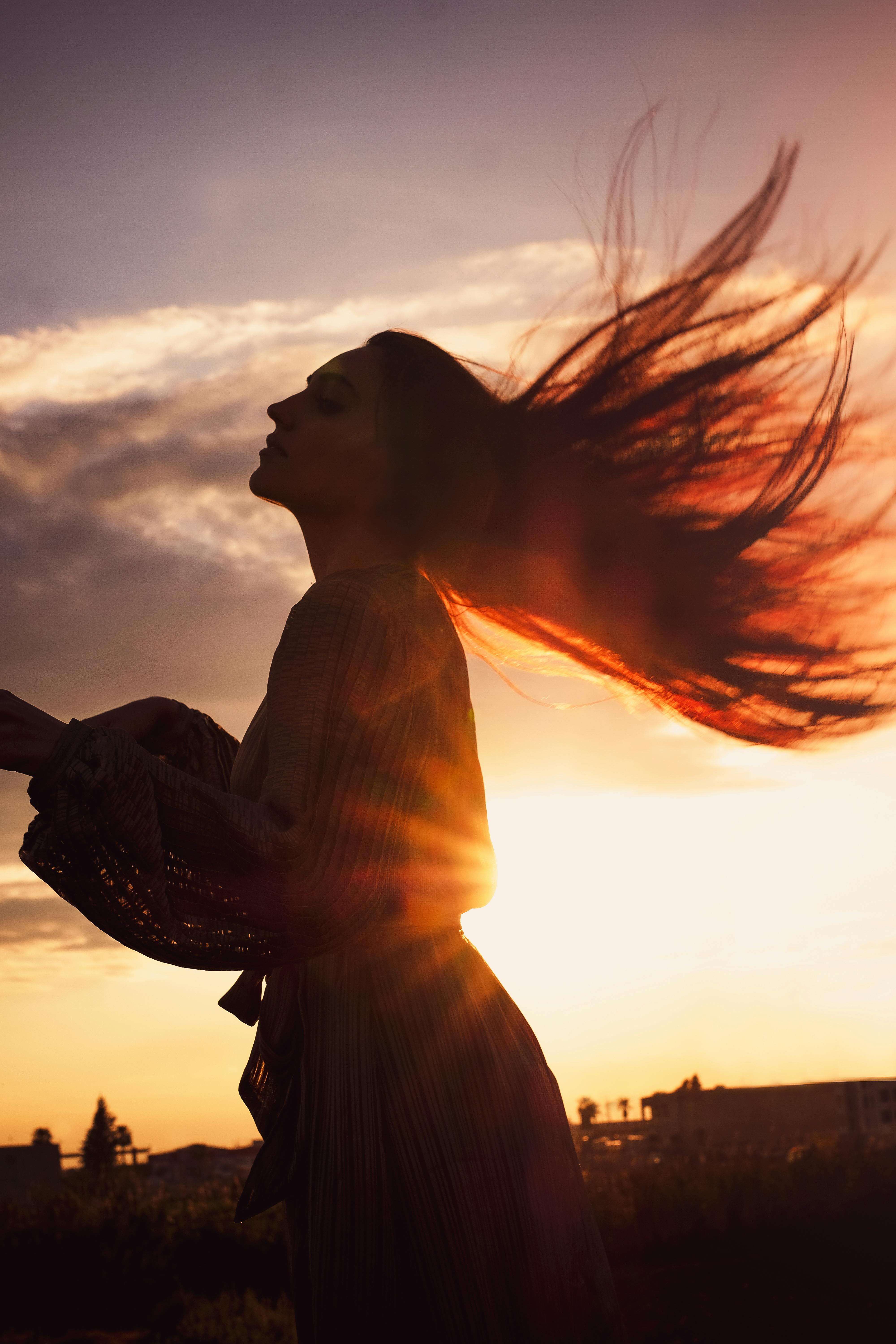 Captivating silhouette of a woman flipping her hair against a vibrant sunset backdrop.