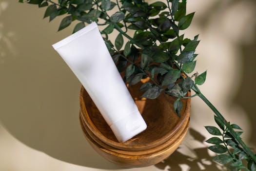 Minimalist skincare tube with green leaves in a wooden bowl, ideal for eco-friendly cosmetic themes.