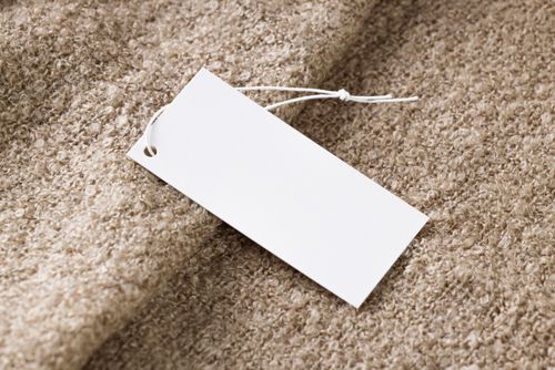 Free Close-up of a blank white price tag on textured beige fabric, ideal for branding use. Stock Photo