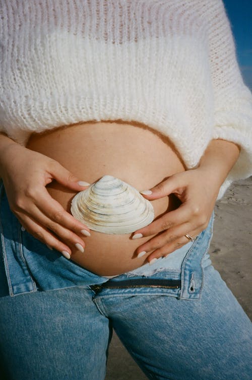 Woman Holding Seashell Over Her Pregnant Belly 