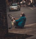 Woman in Blue Jacket and Black Pants Sitting on Sidewalk