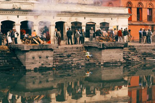 Outdoor scene of a traditional cremation ceremony near a river with a crowd of people.