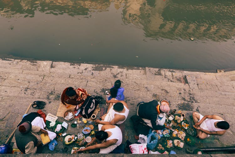 People Eating Near A Murky River