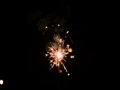 Close-up of a sparkler emitting bright sparks against a dark night sky, creating a mesmerizing effect.