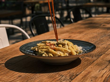 Enjoy creamy penne pasta with vegetables in an outdoor setting. Perfect for a summer meal.