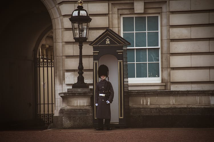 Guard Standing Near The Gate To The Buckingham Palace In London, England 