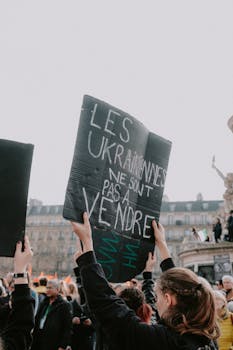 Protesters gather in an urban setting, holding signs for a social cause rally.