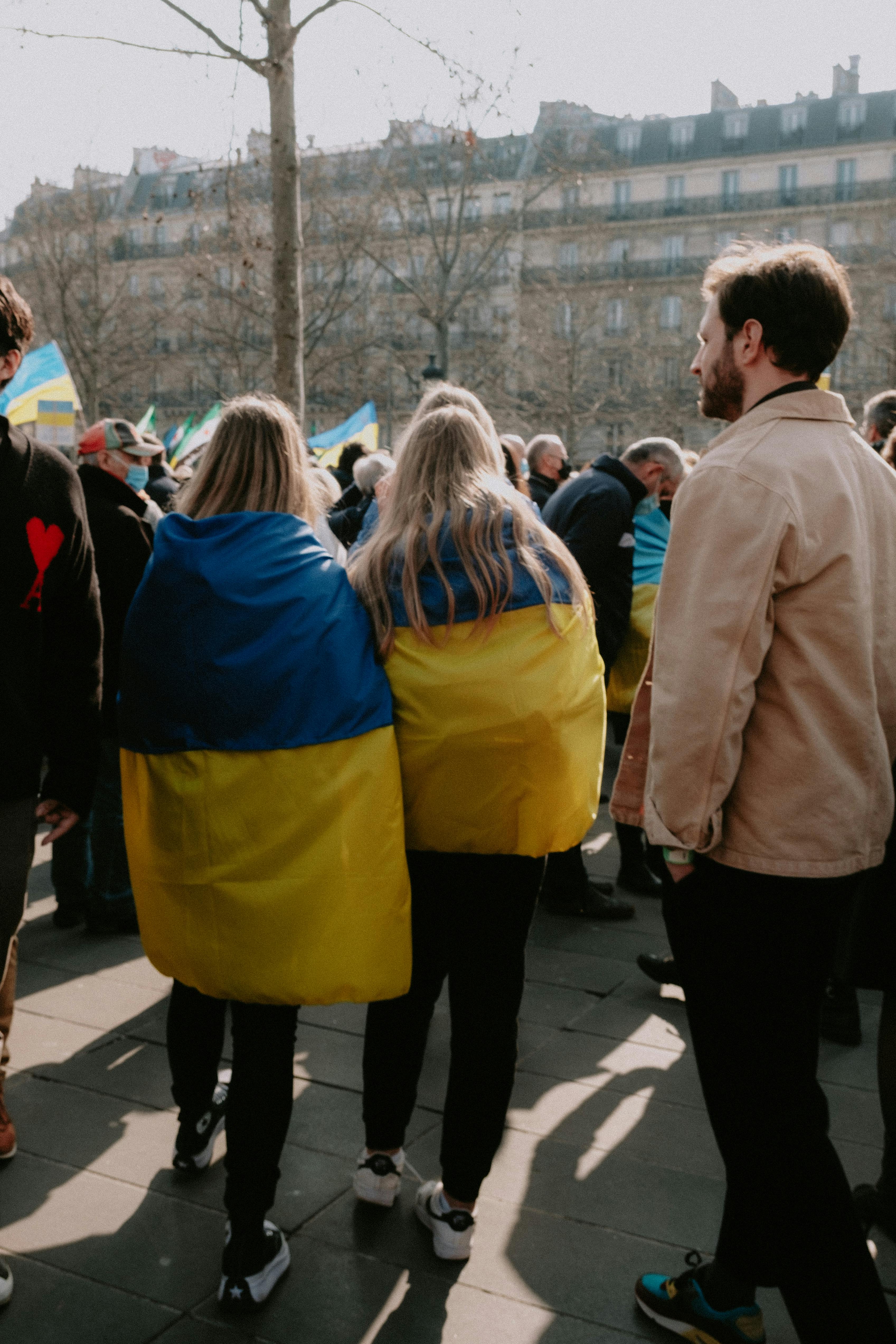 People gathering on a city street wrapped in Ukrainian flags, showcasing solidarity.